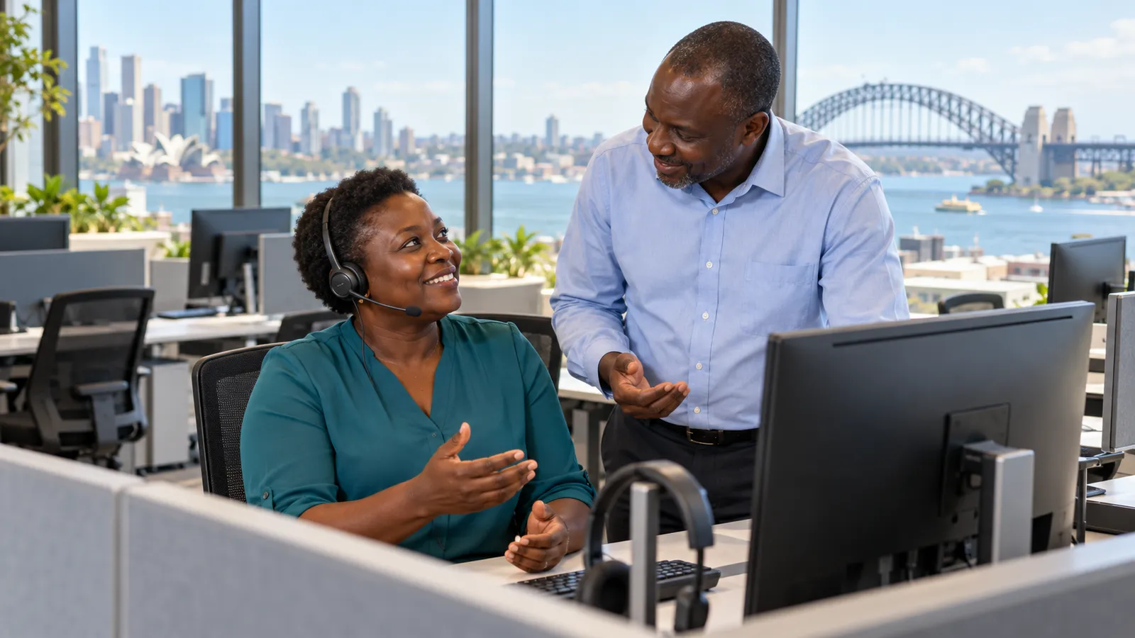 A headset-wearing woman chats with a colleague in a sunlit customer care office overlooking Sydney Harbour.